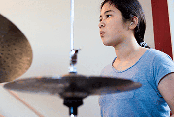 A female musician with hearing aids plays a drum set in the Seattle, WA area.